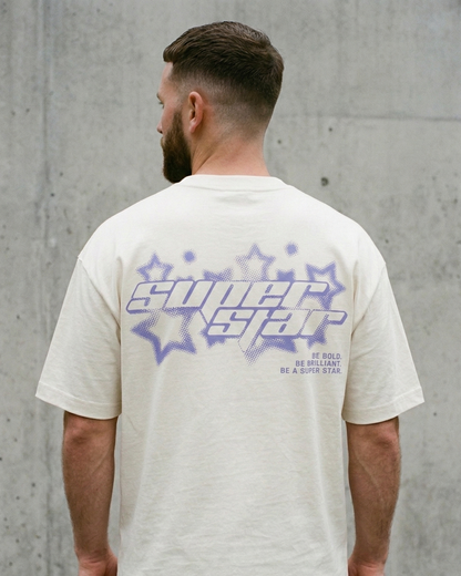 Man wearing a Ivory t-shirt with 'Super Star' design on the back against a gray concrete wall.